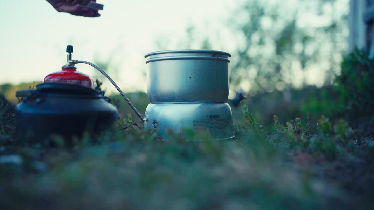 Gros plan sur les mains d'un homme cuisinant sur un réchaud portable en camping près d'iMalitjønna à Indre Fosen, Trøndelag, Norvège.