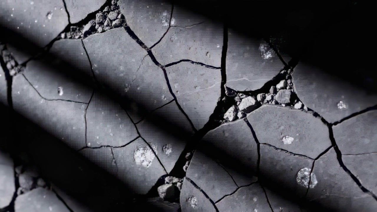 Showing cracked gray surface shifting by sunlight at ground-level, shadow bands with grit in seams