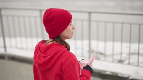 lady in red beanie and hoodie sipping water from pink bottle outdoors drops the water bottle, blurred background of iron rail in serene winter setting