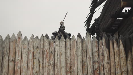 Dark-knight-peeks-behind-high-wooden-fence-on-cloudy-day