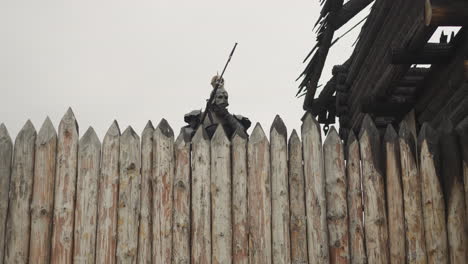 dark knight peeks behind high wooden fence on cloudy day