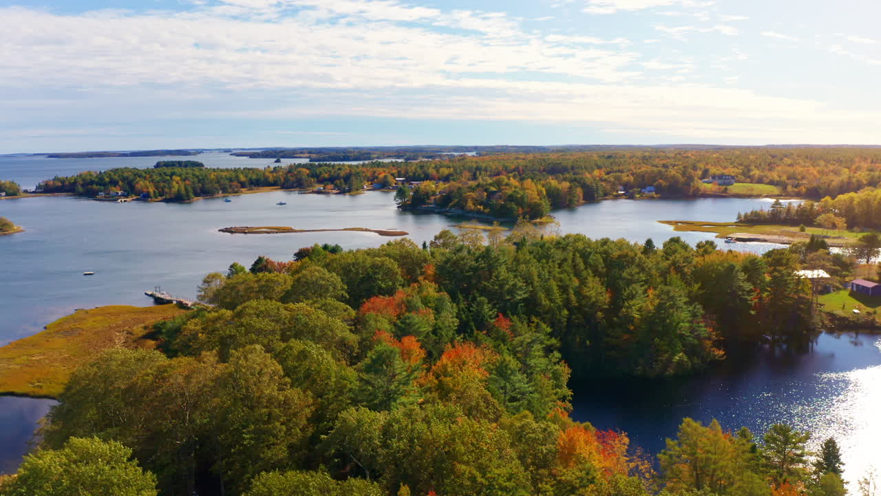 Aerial drone shot over the coastline of Oak Island, Nova Scotia, Canada.
High view of the sea, autumn colorful trees foliage. Picturesque landscape. Fall vibrant colors.