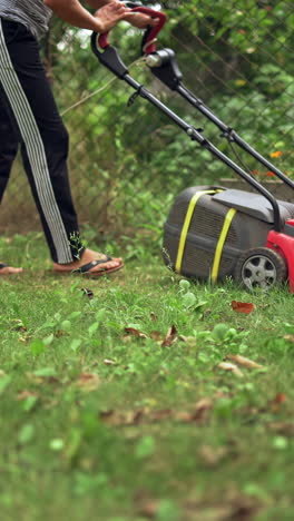 woman working with electic mower machine in the garden. lawn mower cutting green grass outdoors. vertical video
