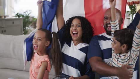 Padres-Birraciales,-Hijo-E-Hija-Viendo-Deportes-En-Televisión-Con-Palomitas-De-Maíz-Y-Bandera-Francesa,-Cámara-Lenta