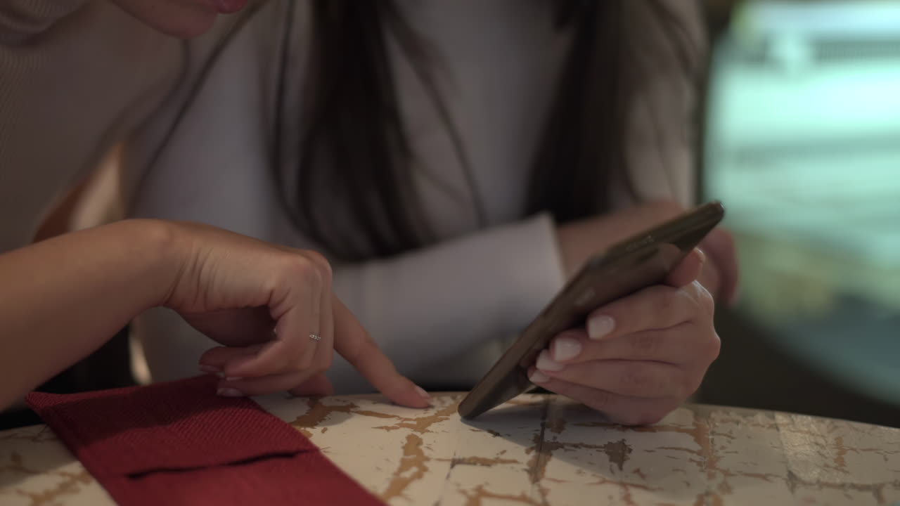 Close up of two women looking at a phone at a table at a cafe