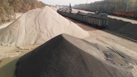 aerial approach into the big rail gravel terminal with heavy machinery unloading wagons with train passes in back