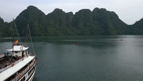 Aerial-drone-shot-of-a-ferry-in-the-water-in-Halong-Bay,-Vietnam-on-a-cloudy-day