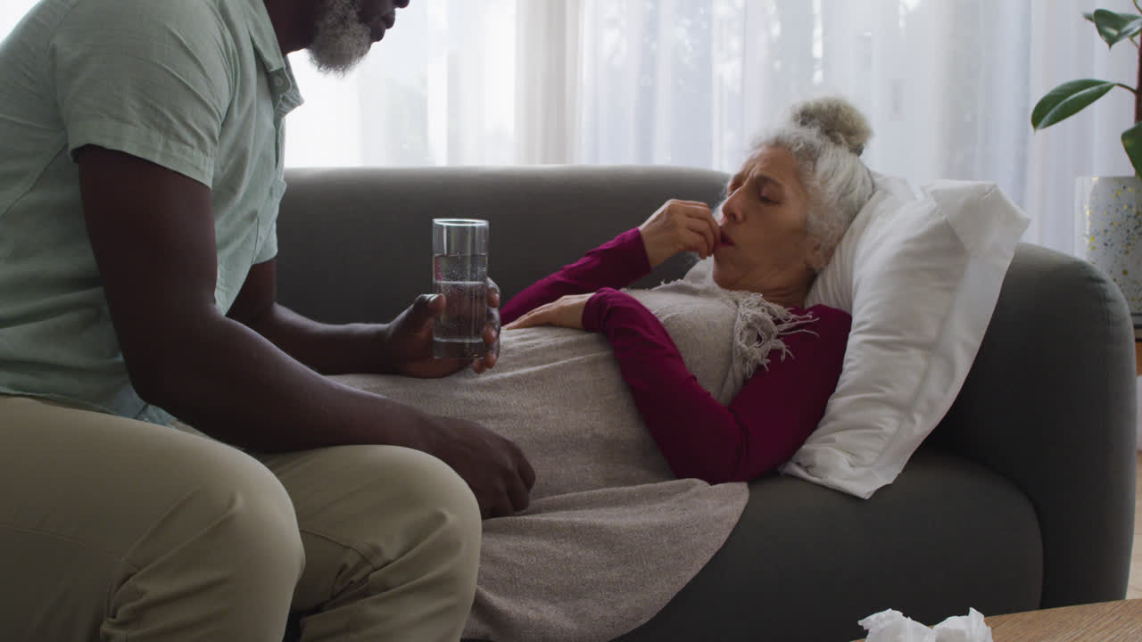 African american man giving medication to his sick wife in the living room at home