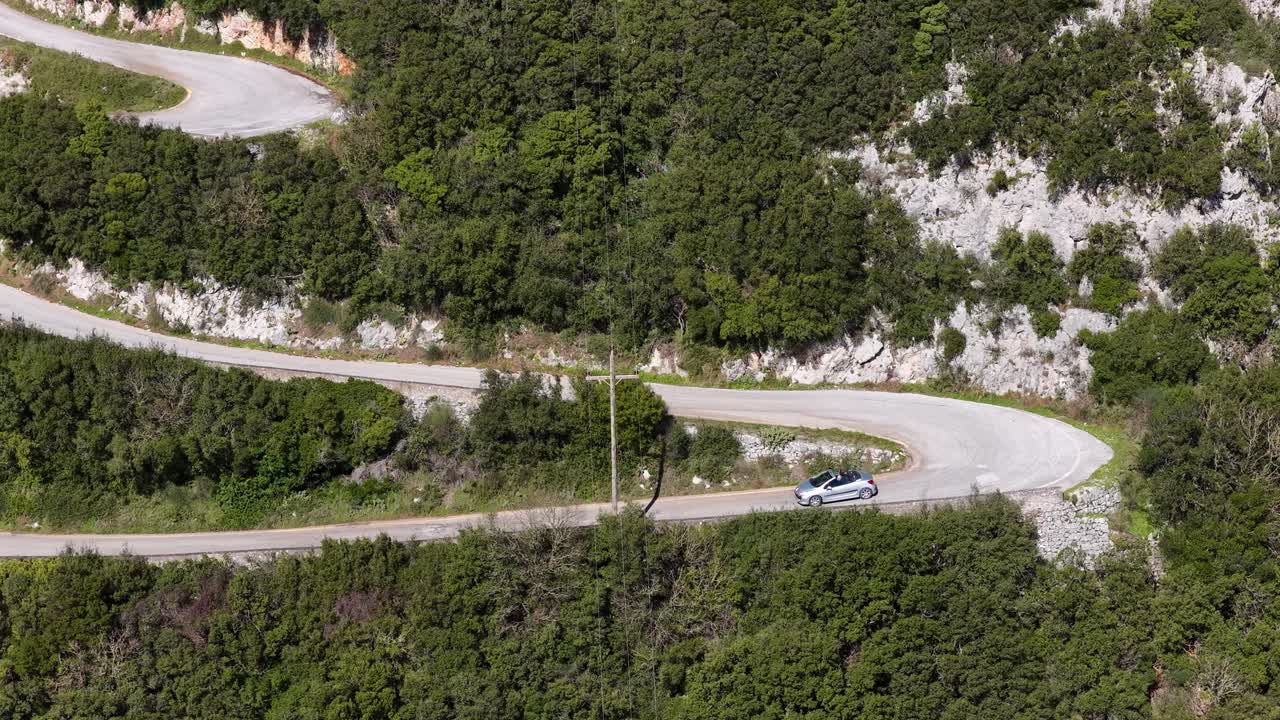 Droneoptagelse fra luften af en cabriolet, der navigerer gennem en hårnålesving på en bjergvej på Korfu.