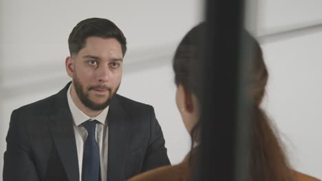 male candidate being interviewed in office for job by female interviewer viewed through window 7