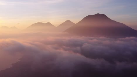 voo épico de drone ao nascer do sol no nível da nuvem sobre san pedro la laguna ao redor do lago atitlan na guatemala, com três vulcões visíveis na foto