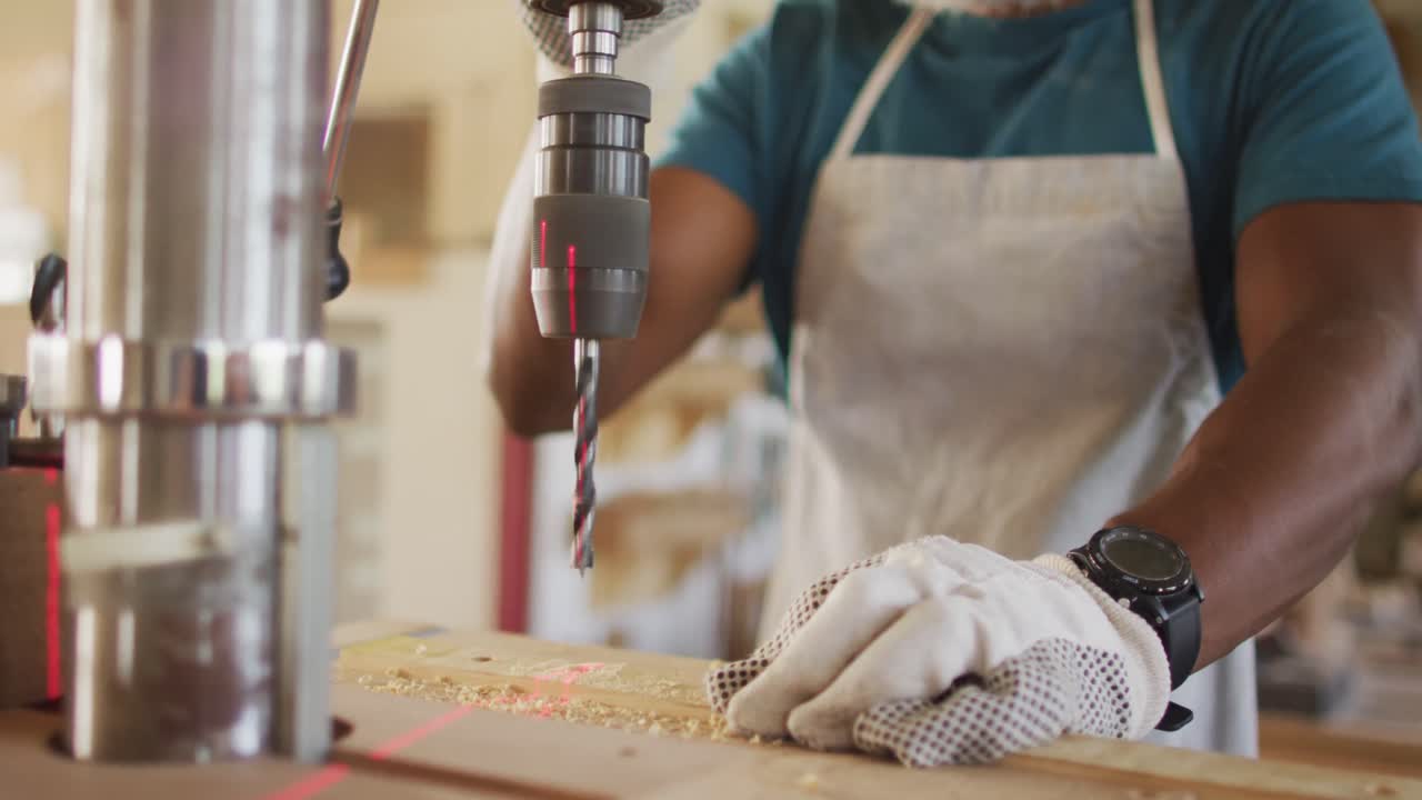Mid section of african american male carpenter drilling wood with a laser drill in a carpentry shop