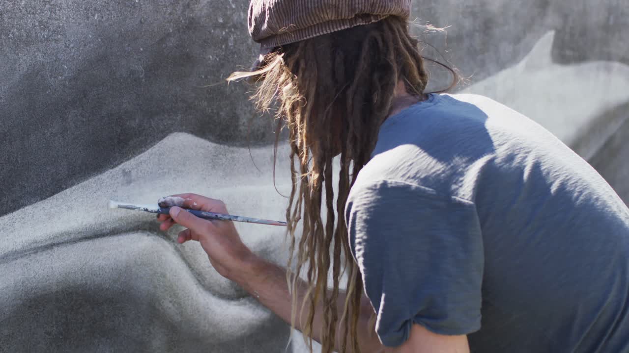 Video of caucasian male artist with dreadlocks painting whale mural on wall