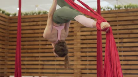 chica en forma vestida con leggins ajustados y top rosa practicando fly yoga-fitness