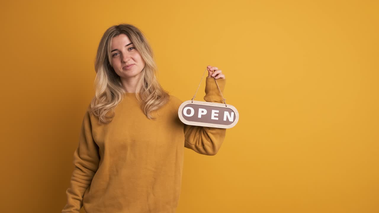 Happy young woman standing and showing open signboard on yellow background