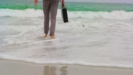 Unterer-Teil-Eines-Geschäftsmannes,-Der-Barfuß-Mit-Aktentasche-Am-Strand-Läuft-4k