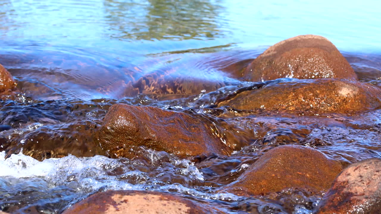 Calm scene as fresh water of stream flows over smooth wet brown rocks