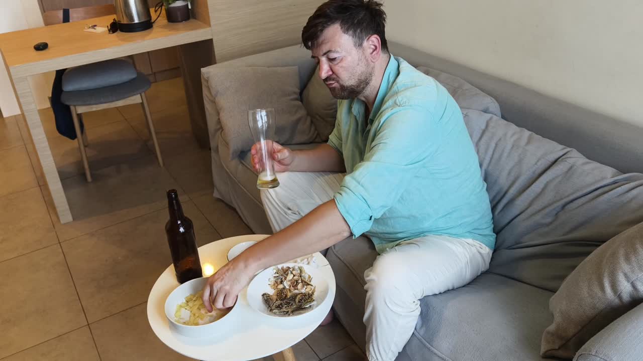 A man relaxing on a sofa with beer and snacks