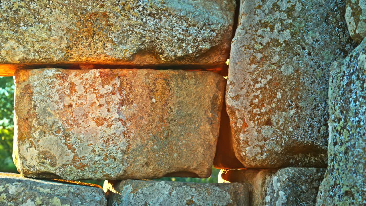 Close-up view of ancient stone blocks, capturing the texture and detail of the weathered surface, with sunlight peeking through the gaps. 8k