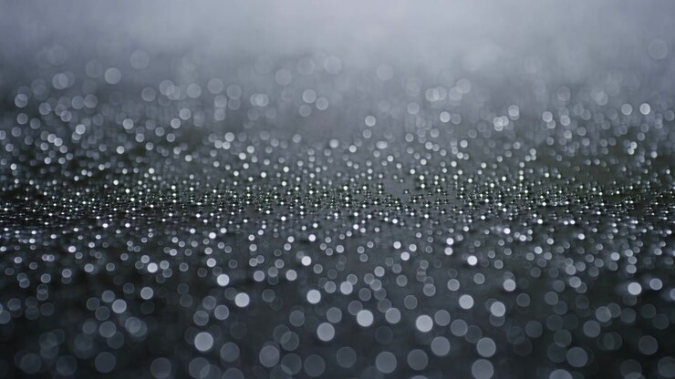 Shallow depth close-up showing a narrow band of sharp rain droplets splashing on a dark horizontal surface. Soft cool-toned lighting creates blurred circular
