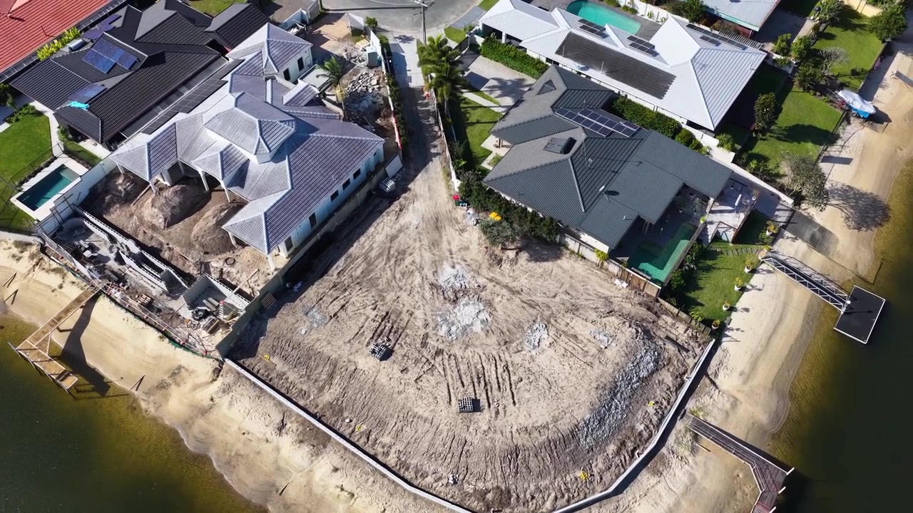 High-angle drone shot shows residential development on a canal waterfront under bright daylight.