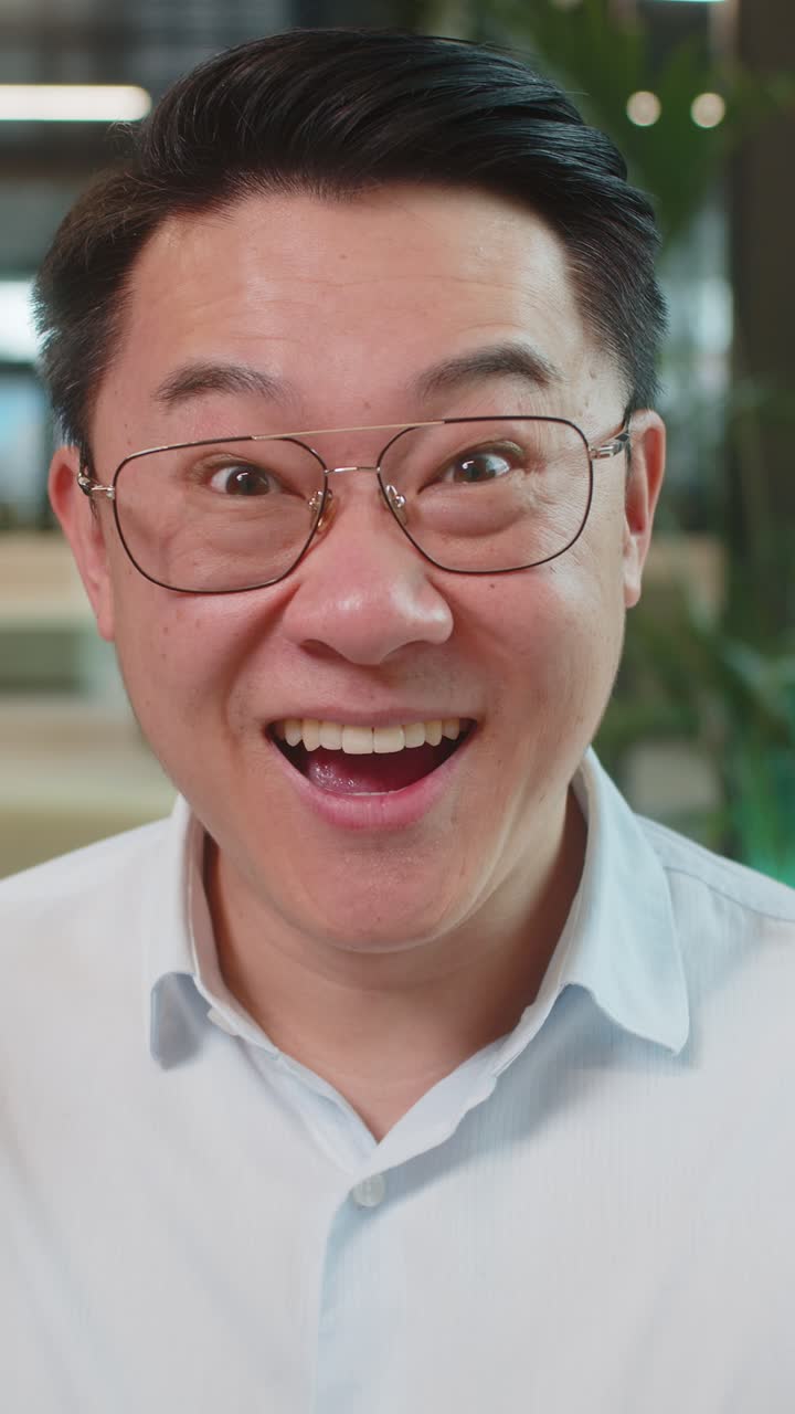 Chinese young businessman in shirt looking at camera shocked by sudden victory in office lobby