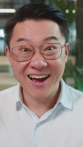 Chinese young businessman in shirt looking at camera shocked by sudden victory in office lobby