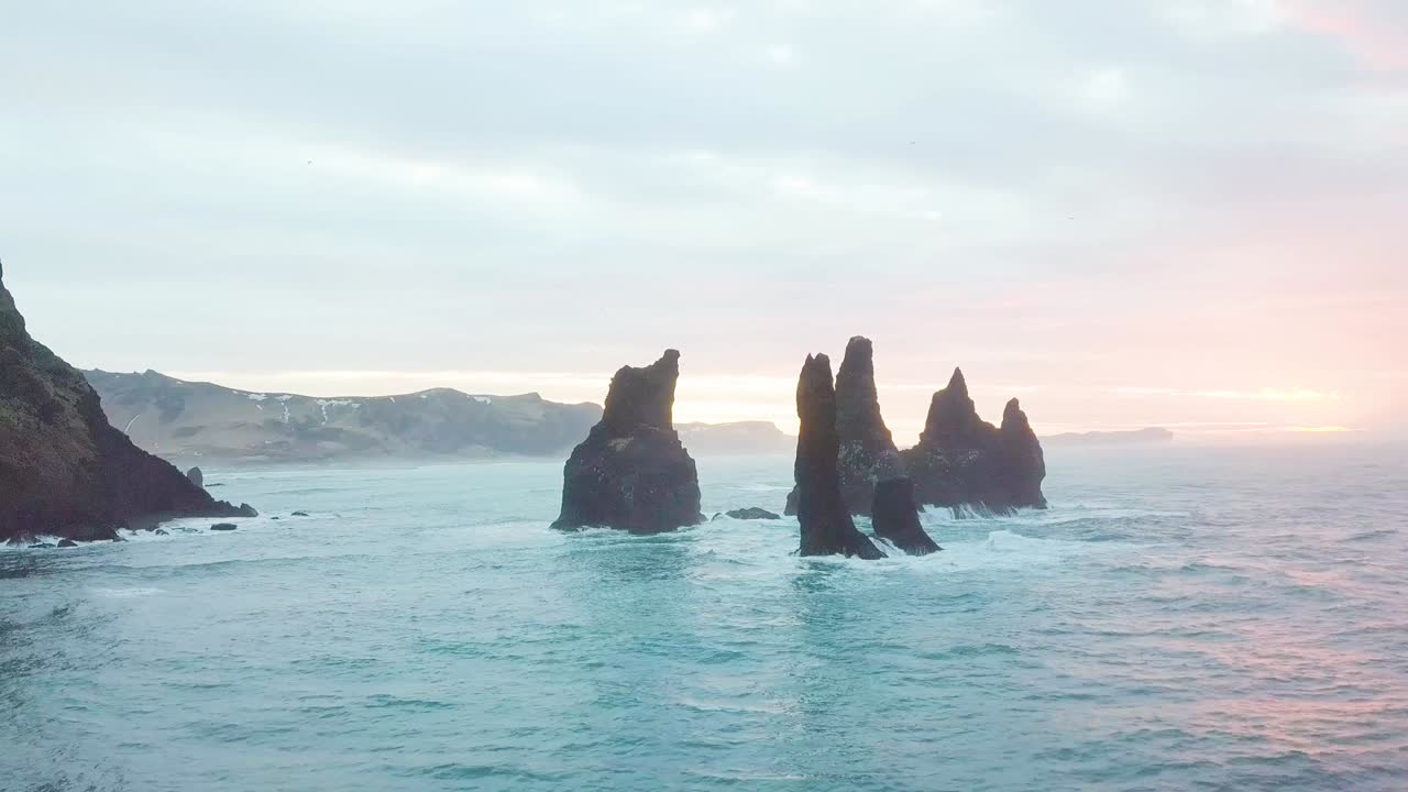 아이슬란드 남쪽의 vik i mýrdal 의 reynisfjar 해변에 있는 reynisdrangar 바위, 해가 뜨는 동안 절벽 위를 날아가는 공중 드론 촬영, 큰 폭풍파가 바위에 부히고, 고해상도 영상.