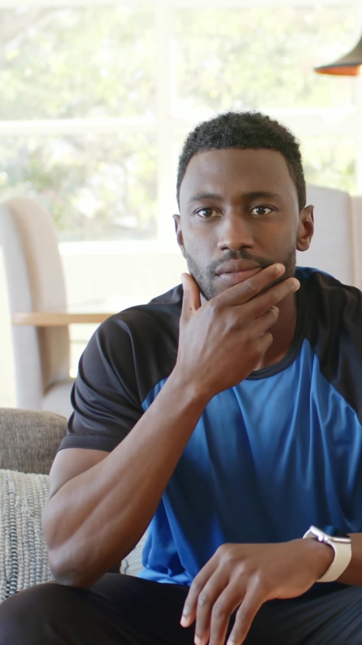 Vertical video: After hearing comment man in blue sport tee thinking and touching watch at home