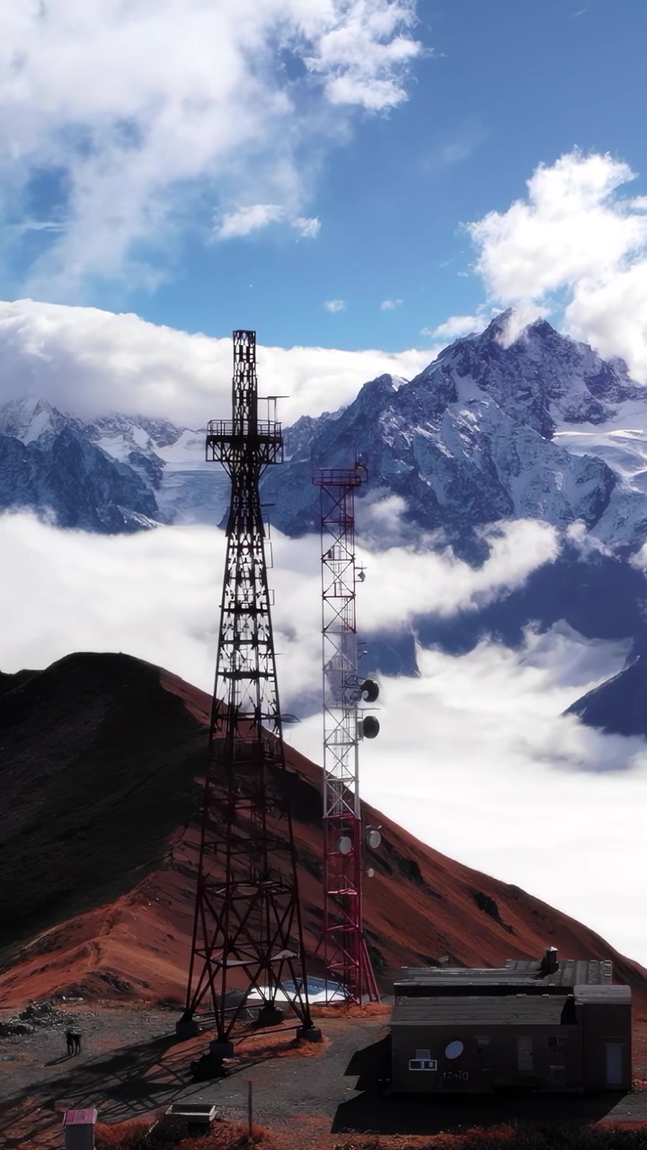 Torre di comunicazione su crinale avvolto dalle nuvole, capanne rustiche per attrezzature e antenne appollaiate sopra un mare di nebbia