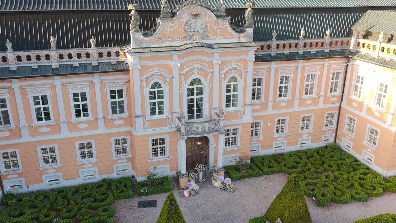 Ilmakuva Nové Hrady -linnan sisäänkäyntiportista ja puutarhoista. Aurinkoinen dronekuva, joka esittelee eleganttia barokkimaista maisemaa.