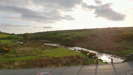 coche rojo llegando a una intersección con un puente de piedra medieval durante el atardecer en dartmoor, inglaterra