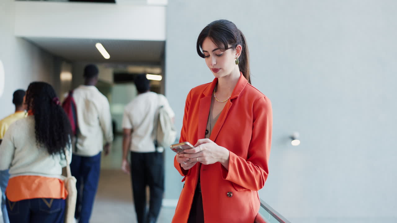 Wanita Muda Mengenakan Blazer Merah Menggunakan Smartphone di Gedung Modern
