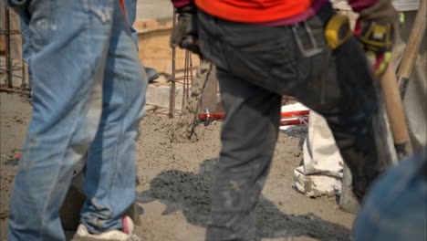 langsame nahaufnahme einer betonmischung, die an einem hellen, sonnigen tag auf einer baustelle gegossen wird, während die arbeiter herumlaufen und sie abflachen