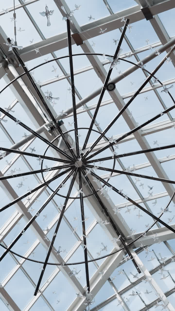 vista gran angular de un moderno techo de vidrio con instalaciones colgantes decorativas en forma de pájaros, con patrones de cuadrícula geométrica y luz natural brillante del cielo de arriba