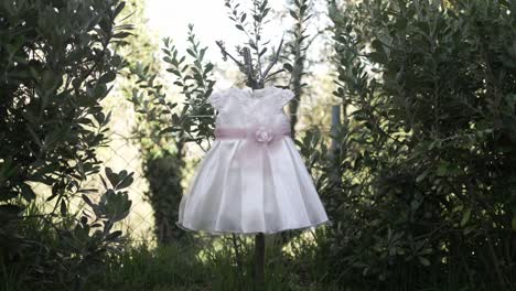baby dress with floral belt hanging between green bushes outdoors, soft light