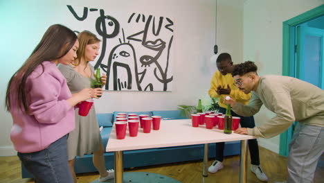 happy multiethnic young friends playing beer pong at home