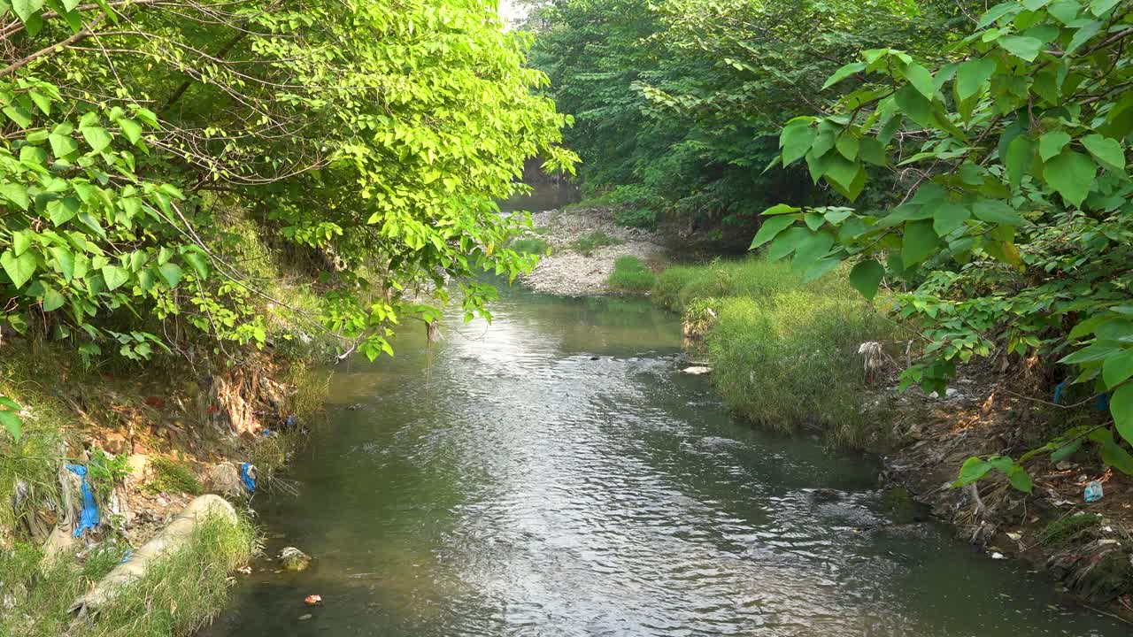 Water flows through the town, but garbage and waste pollute the environment. We must take action to clean up our surroundings and protect our community.