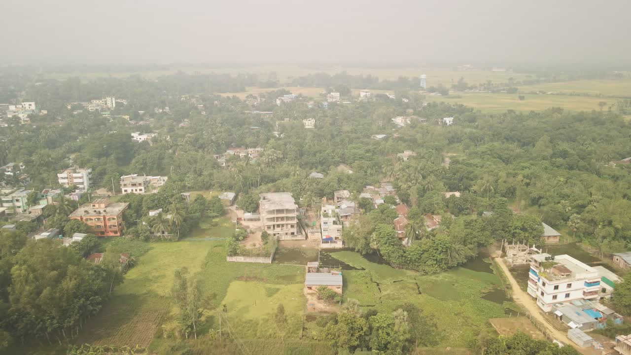 Drone lifts up and moves backward, unveiling a serene rural village in Bangladesh with scattered houses and lush greenery.