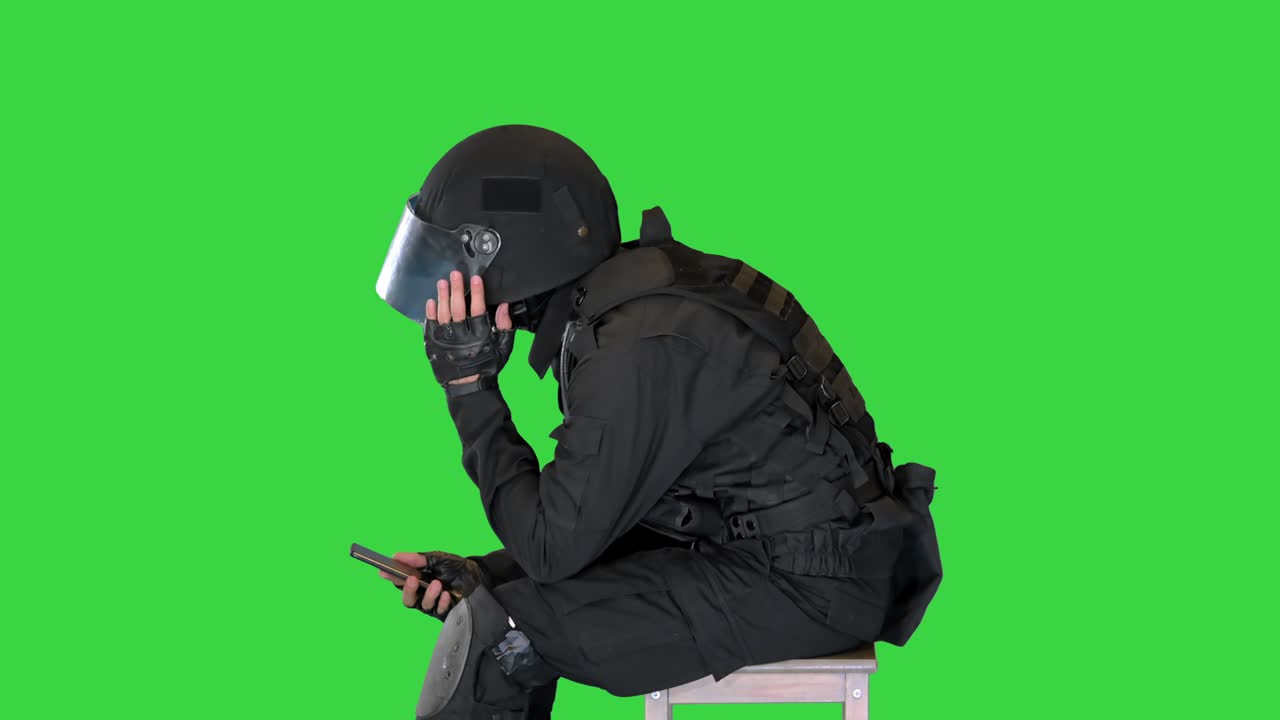 policía táctico sacudiendo la cabeza leyendo noticias en el teléfono inteligente en una pantalla verde, clave de croma