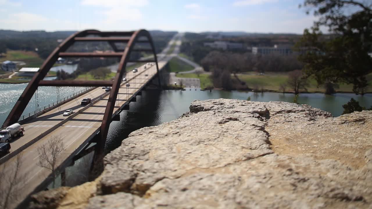 Austin Pennybacker Bridge tilt-shifted time-lapse, focus isolates section of ledge and front part of the bridge. Heavy traffic flow northbound and traffic backs up once light changes.