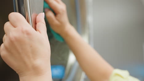 hand of laundry janitor wiping transparent surface door of washing machine with blue soapy towel, reflection visible on glass, detailed close up of cleaning action in laundromat interior