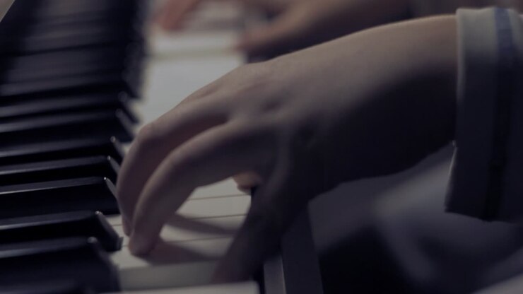 Nuori poika soittaa pianoa, käsien lähikuva musiikkikappaleen päättyessä