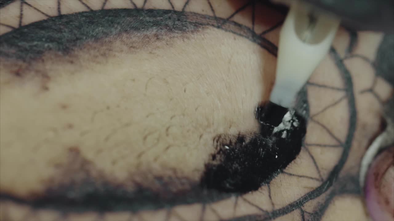 Tattoo artist applying black ink to a tattoo design