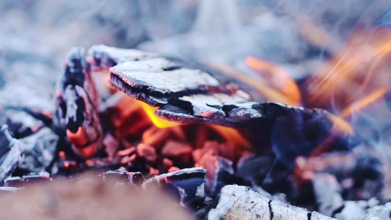 Close-up of glowing campfire embers with smoke rising, evoking warmth, nostalgia