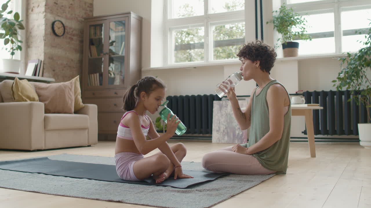 madre e hija haciendo yoga en casa y bebiendo agua