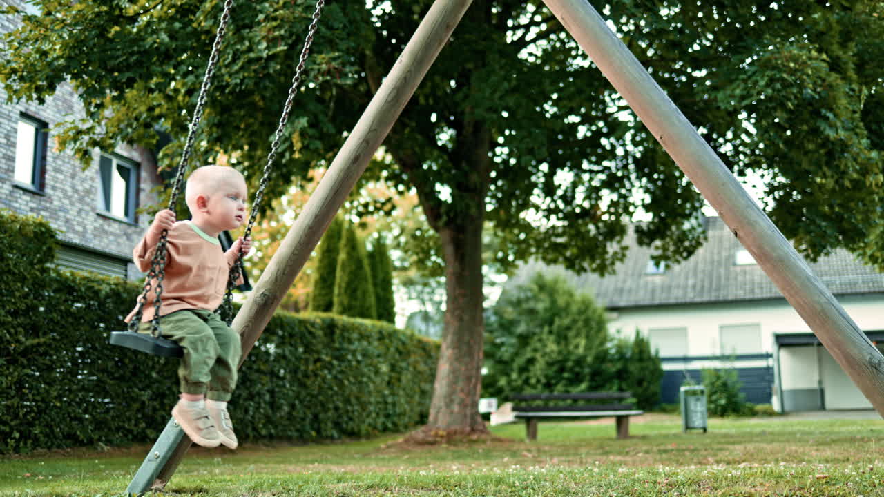 Happy boy swings on a swing on a playground in the park. The child has fun on a walk. Swing for children in a city park. Toddler boy rides on a swing in the summer. Children's entertainment