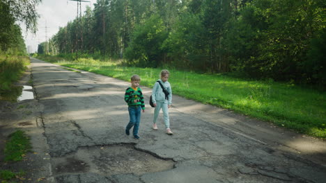 young boy holding flower walks beside sister wearing bag as they enjoy peaceful moment along cracked paved path surrounded by lush green forest under soft daylight in natural setting