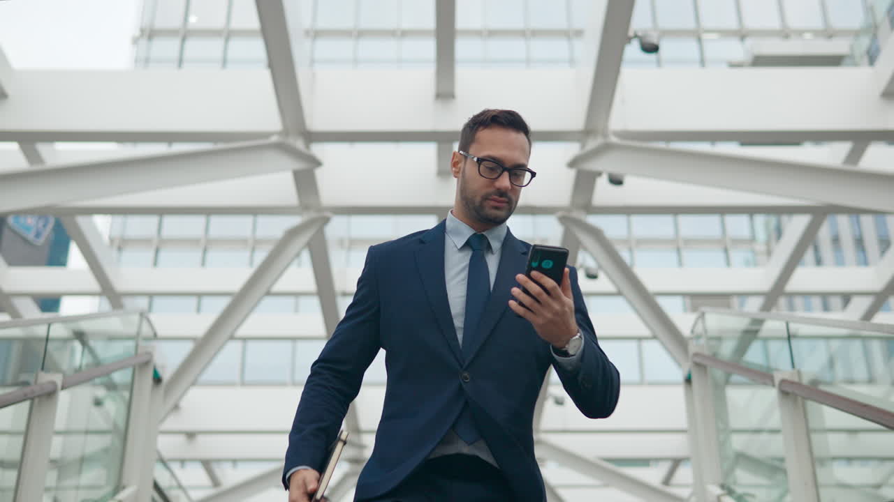 un hombre de negocios baja las escaleras con un cuaderno en la mano y lee un mensaje en el teléfono mientras está en movimiento.
