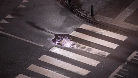 Toma-En-ángulo-Alto-De-Gotas-De-Lluvia-En-Un-Charco-En-El-Cruce-Peatonal-En-La-Calle-De-La-Ciudad-Por-La-Noche